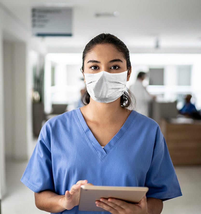 Nurse-wearing-a-mask-and-holding-a-digital-tablet-at-a-clinic