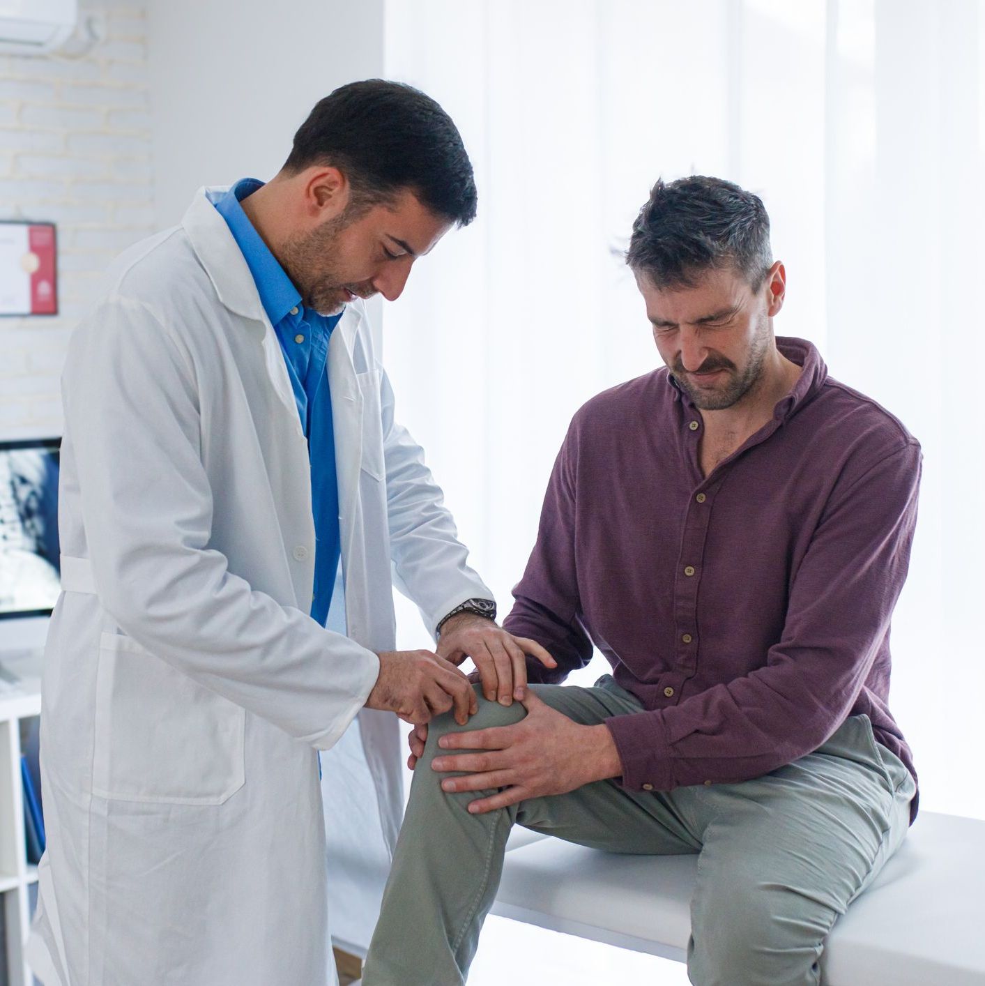 Doctor checking knee joint of male patient