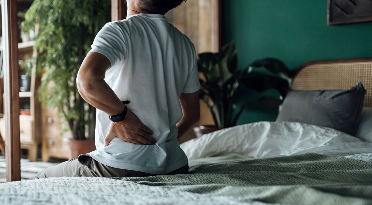 person-sitting-on-the-edge-of-a-bed-holding-their-lower-back