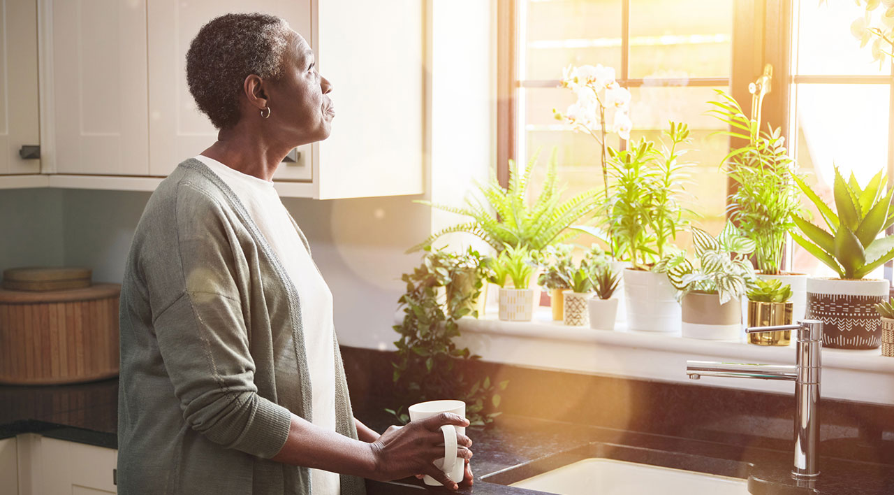 senior-woman-having-a-cup-of-coffee-in-the-kitchen-and-looking-out-of-her-window