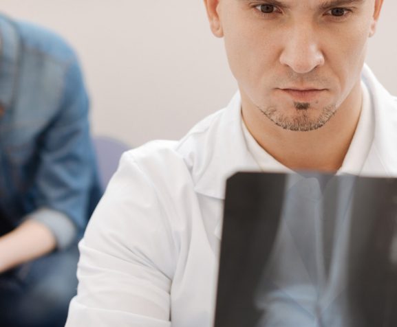 Serious-experienced-male-rheumatologist-holding-at-X-ray